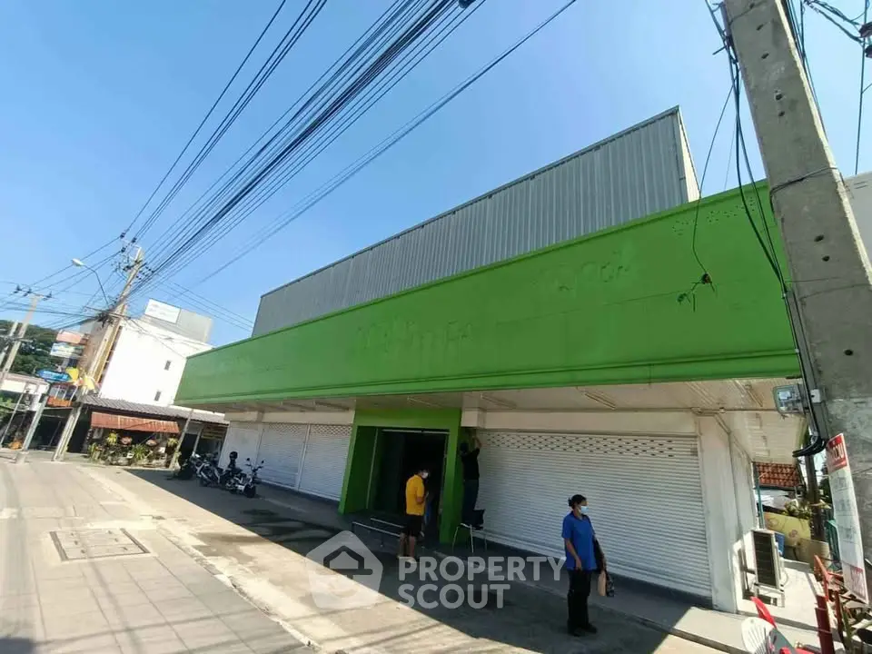 Commercial building with green facade and closed shutters on a sunny day.