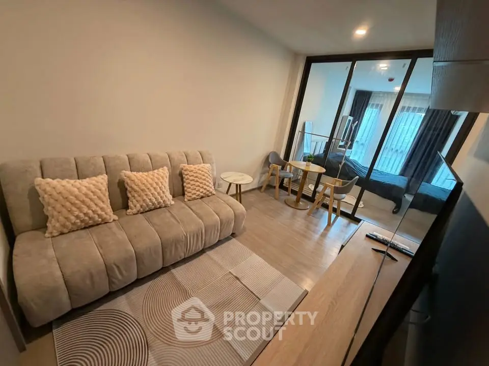 Modern living room with stylish sofa and glass partition leading to bedroom, featuring elegant decor.