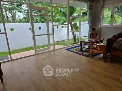 Spacious living room with large windows and garden view, featuring wooden furniture and elegant rug.