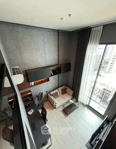 Modern loft-style living room with high ceiling and large windows offering city views.