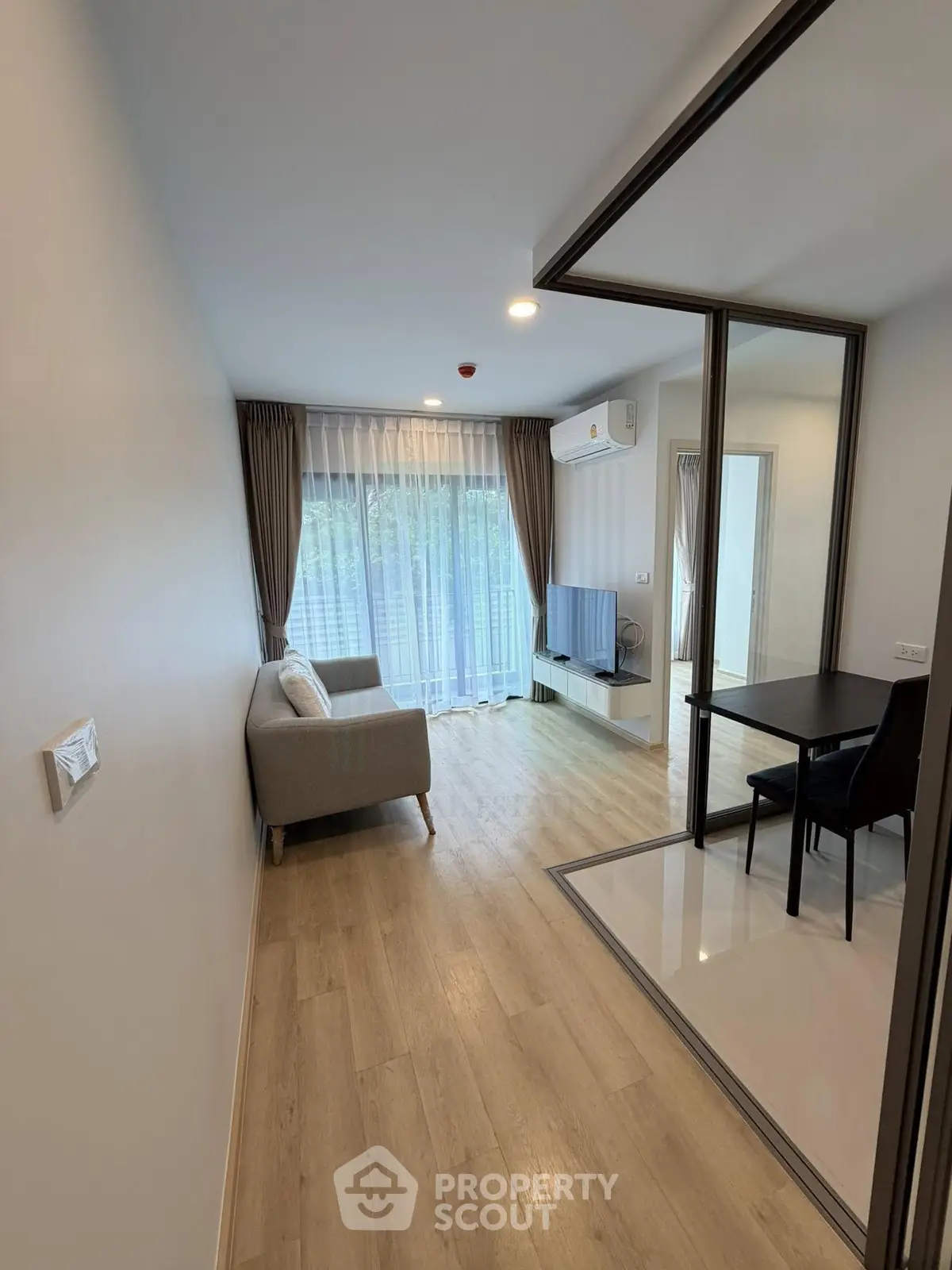 Modern living room with wooden flooring and large window, featuring a cozy sofa and TV setup.