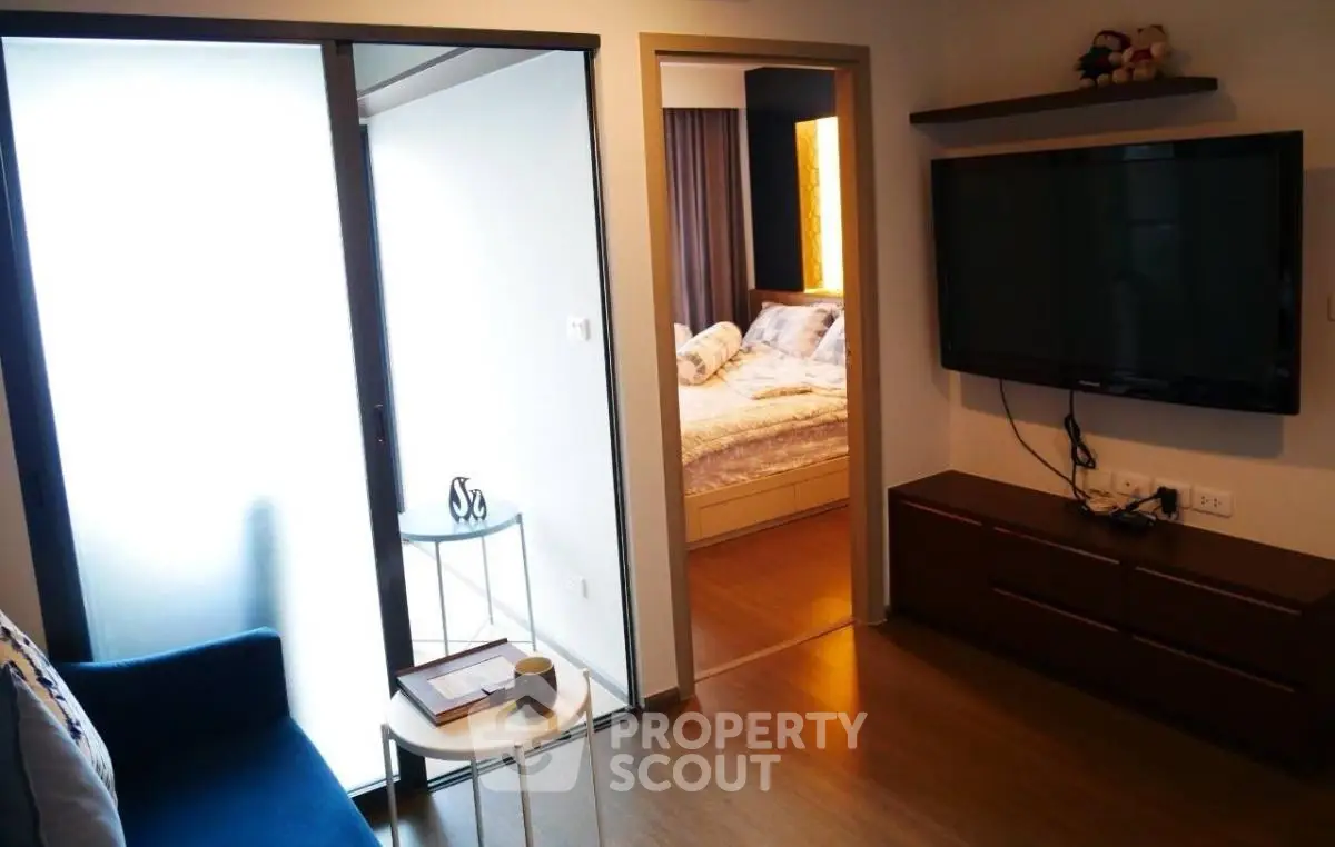 Cozy living room with modern TV setup and view into a stylish bedroom