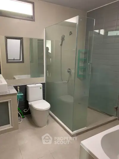 Modern bathroom with glass shower, bathtub, and sleek fixtures in a contemporary home.