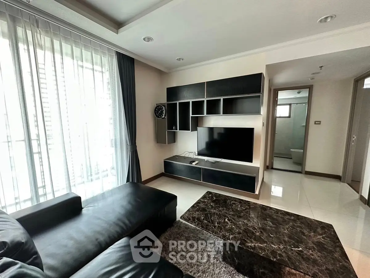 Modern living room with sleek black furniture and large TV, featuring natural light from floor-to-ceiling windows.