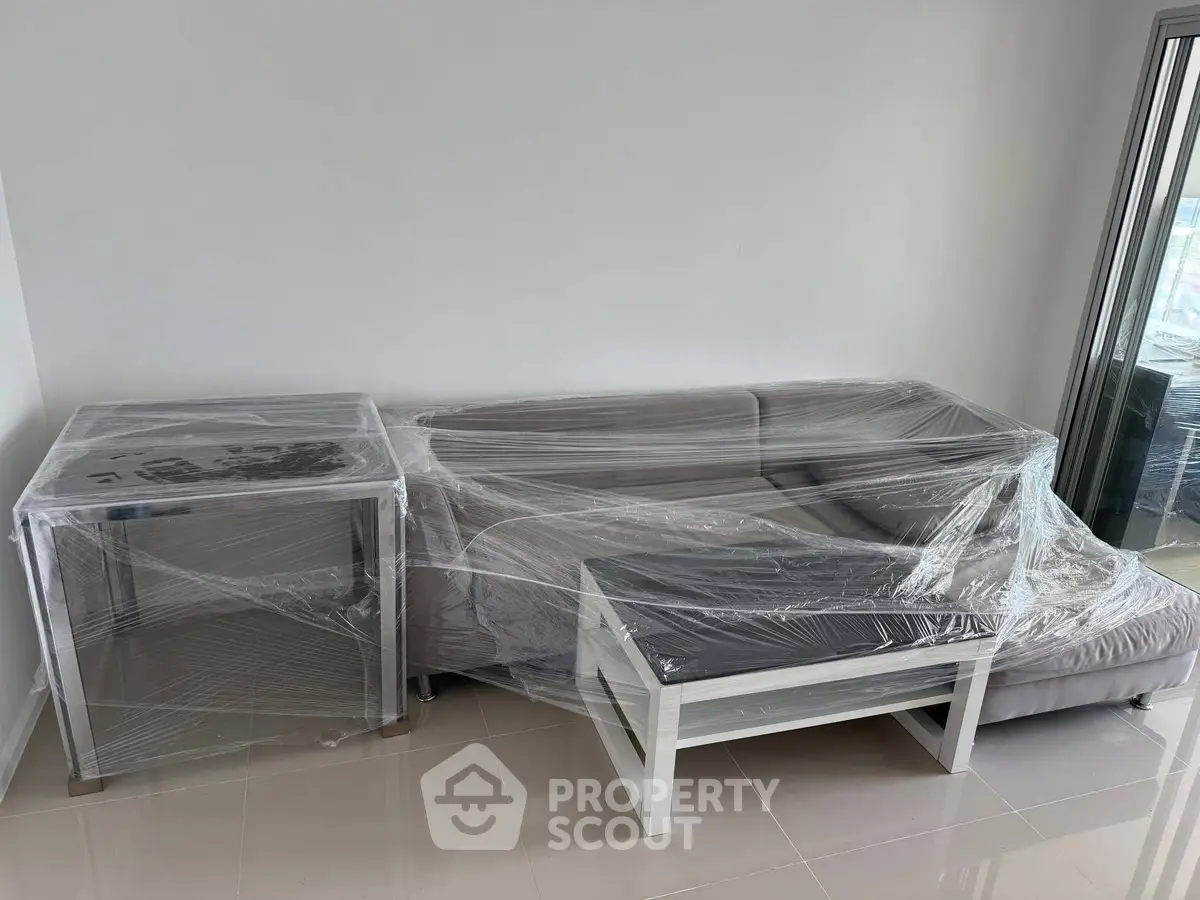 Modern living room with wrapped furniture and large windows offering natural light.