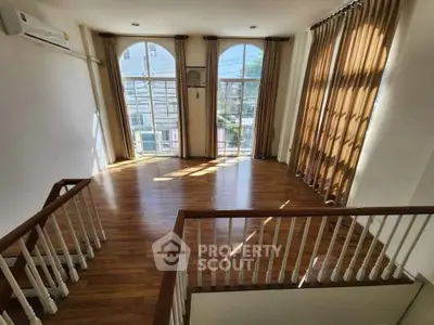 Spacious sunlit living room with elegant wooden flooring and large windows.