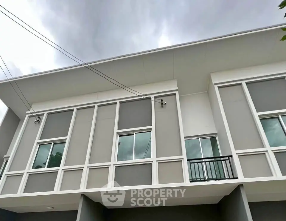 Modern townhouse exterior with sleek design and large windows under a cloudy sky.
