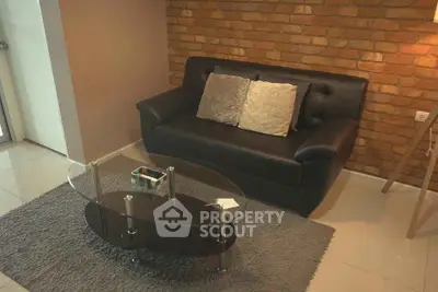 Cozy living room with modern black sofa and glass coffee table on a plush rug, brick accent wall.