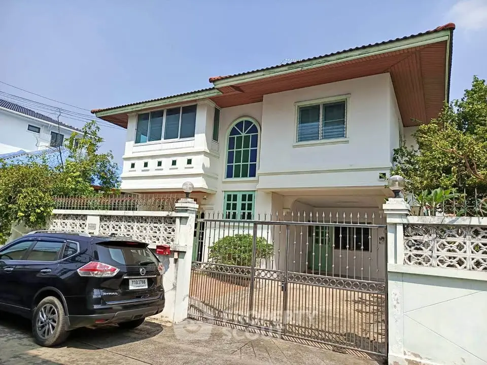 Charming two-story house with gated driveway and lush greenery, perfect for family living.