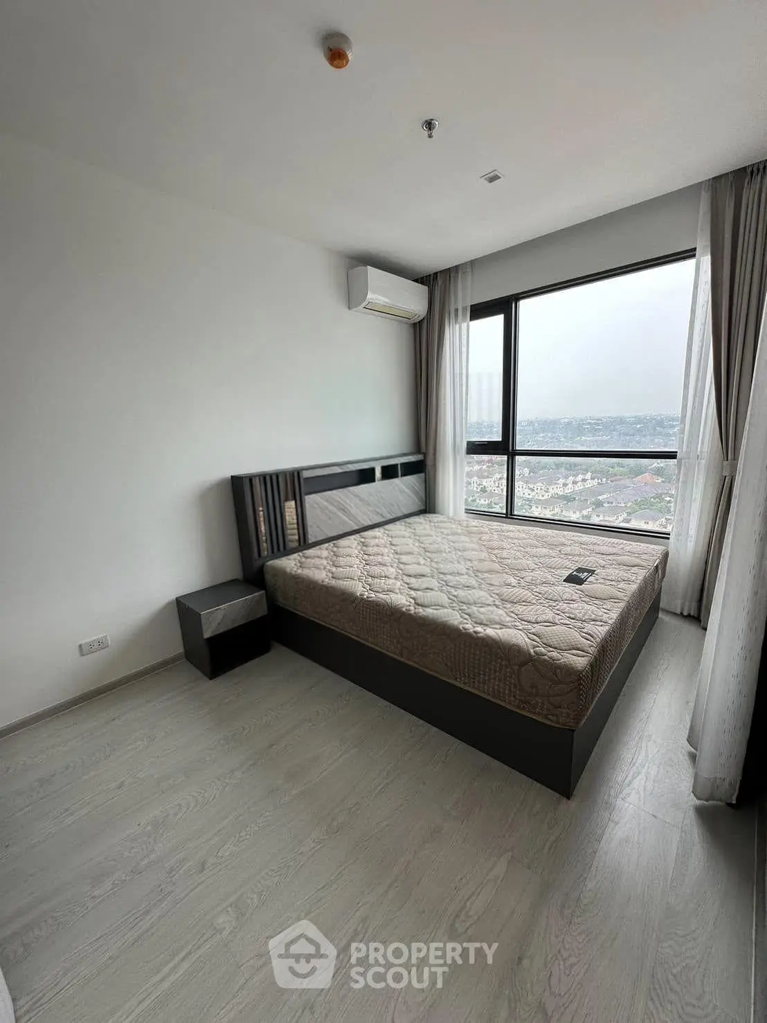 Spacious bedroom with large window offering stunning city views, modern furnishings, and ample natural light.