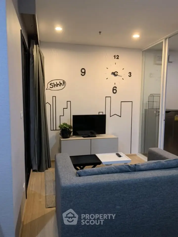 Modern living room with stylish wall clock and cityscape decor, featuring a cozy gray sofa and sleek TV setup.