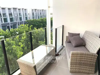 Charming balcony with cozy seating and glass railing overlooking lush greenery in modern apartment complex.