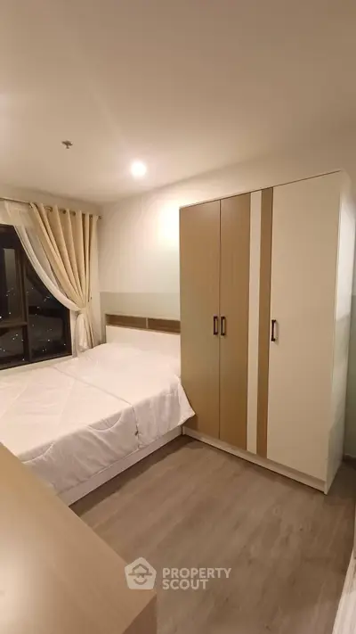 Cozy bedroom with modern wardrobe and large window offering city views.