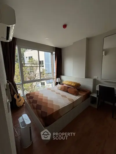 Cozy bedroom with large window, modern furnishings, and natural light in urban apartment.