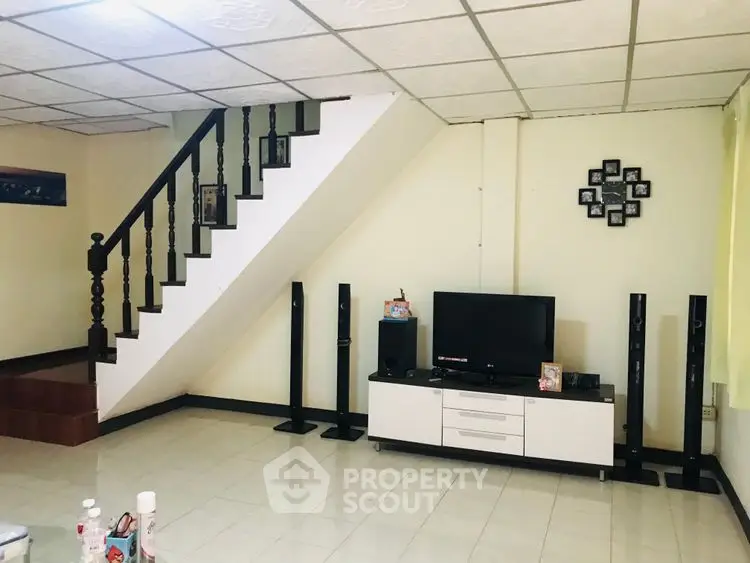 Spacious living room with modern entertainment setup and elegant staircase.