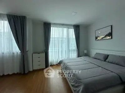 Spacious bedroom with large windows and elegant decor, featuring a comfortable bed and stylish curtains.
