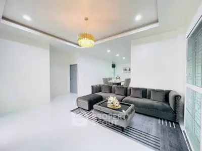 Spacious modern living room with elegant chandelier and plush gray sofa.