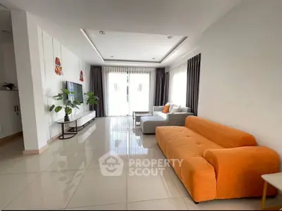 Spacious modern living room with bright orange sofa and large windows for natural light.