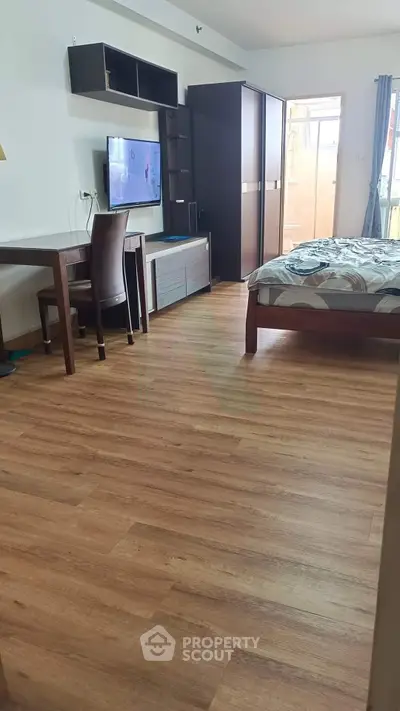 Spacious bedroom with modern furnishings and wooden flooring, featuring a TV and ample storage space.