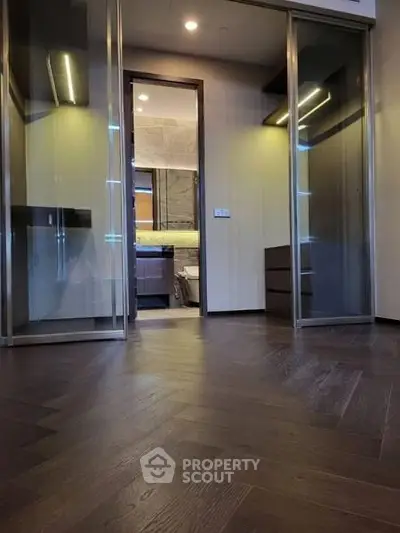 Luxurious modern interior with sleek wooden flooring and glass doors leading to a stylish bathroom.