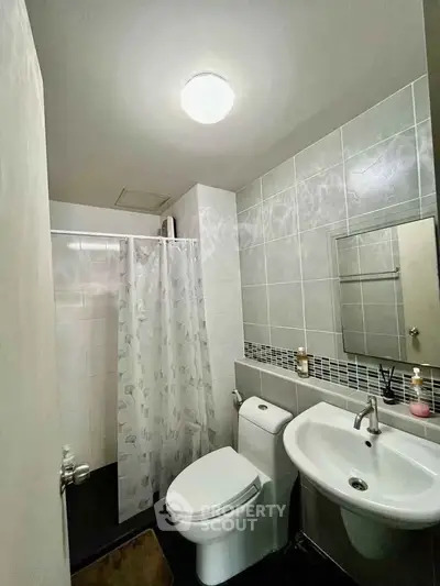 Modern bathroom with sleek fixtures and tiled walls, featuring a shower and compact sink.