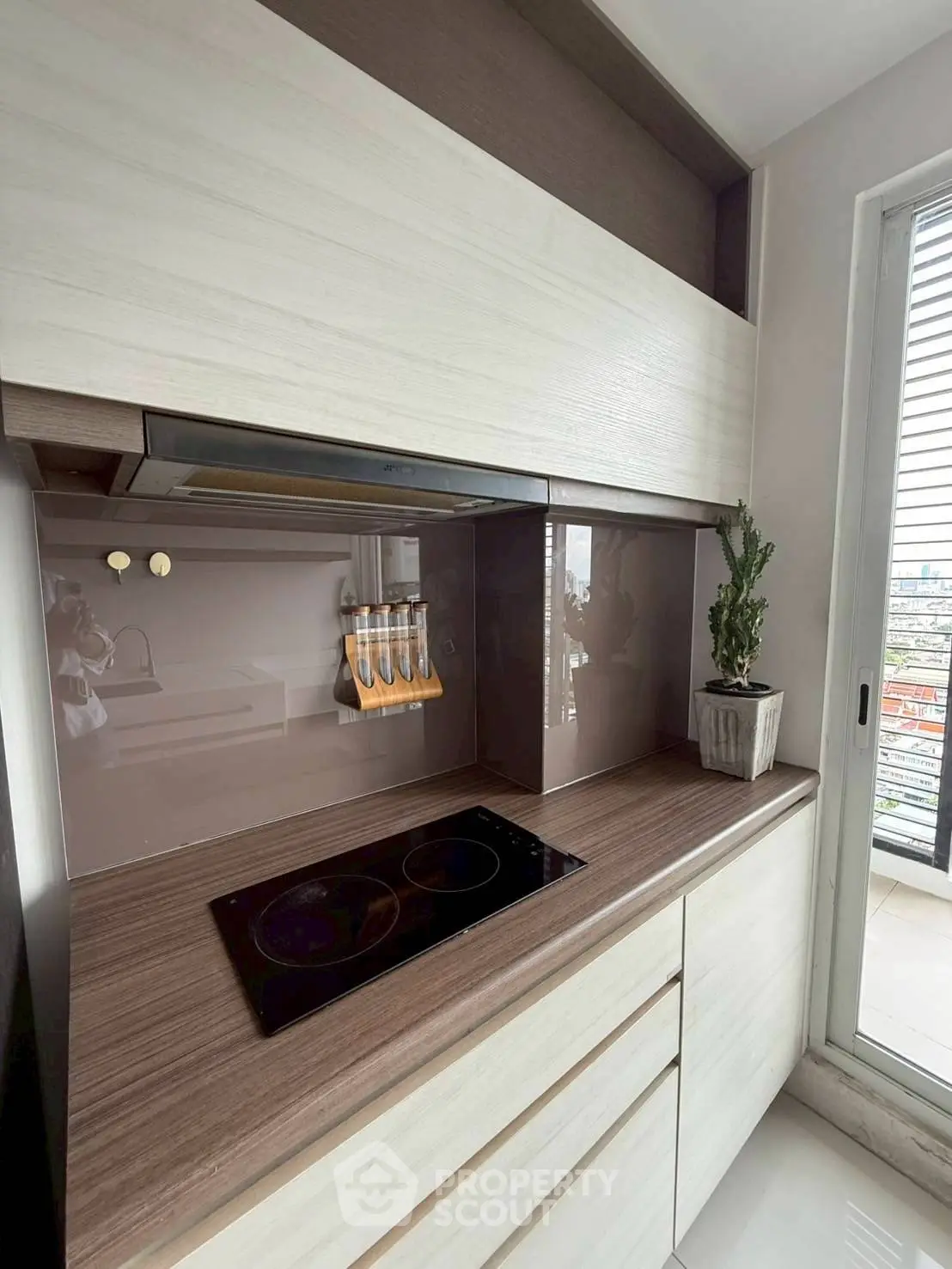 Modern kitchen with sleek cabinetry and electric cooktop, featuring a small balcony view.