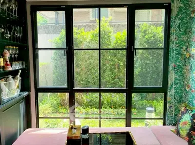 Charming living room with large windows overlooking lush garden, featuring elegant decor and natural light.