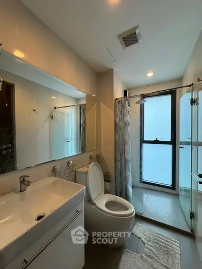Modern bathroom with glass shower and large mirror in sleek apartment.