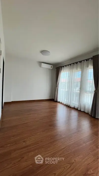 Spacious empty room with wooden flooring and large windows, perfect for customization.