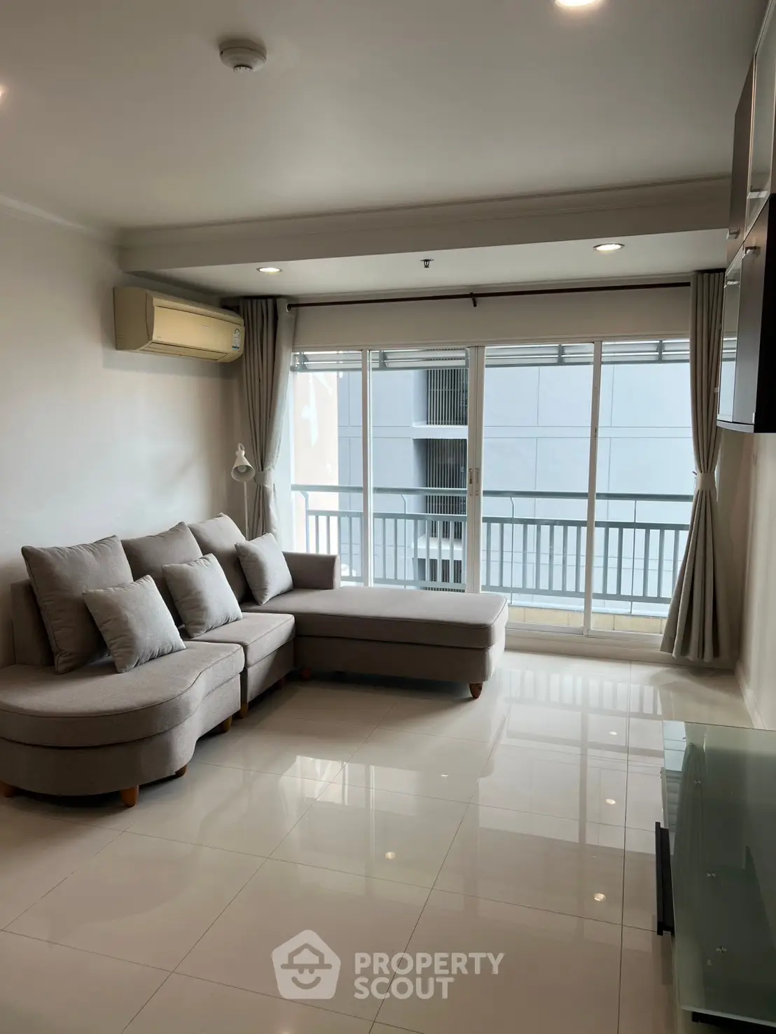Spacious living room with modern sofa and large windows leading to a balcony, offering ample natural light.