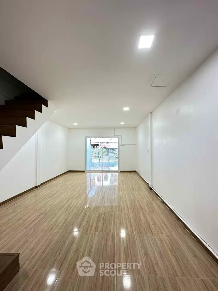 Spacious open-plan living room with sleek wooden flooring and modern staircase, perfect for contemporary living.