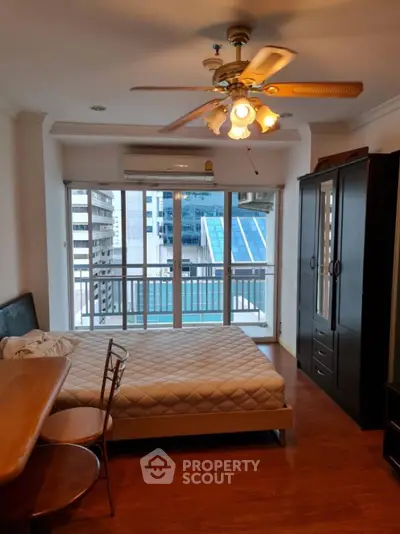 Spacious bedroom with city view, wooden flooring, and ceiling fan in modern apartment.