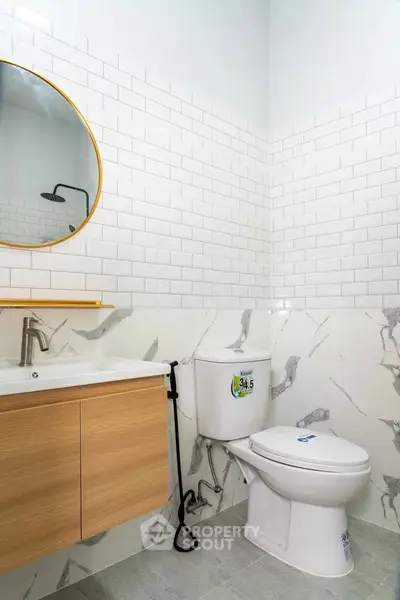 Modern bathroom with stylish fixtures and marble accents, featuring a round mirror and sleek vanity.