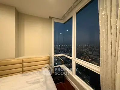 Luxurious bedroom with stunning city view from high-rise window at dusk.