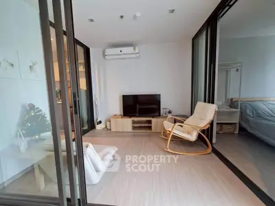 Modern living room with sliding glass doors, cozy seating, and a TV unit, adjacent to a bedroom.