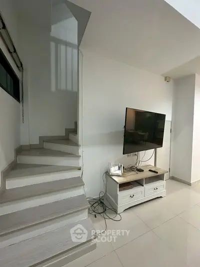 Modern living room with sleek staircase and mounted TV, perfect for contemporary living.