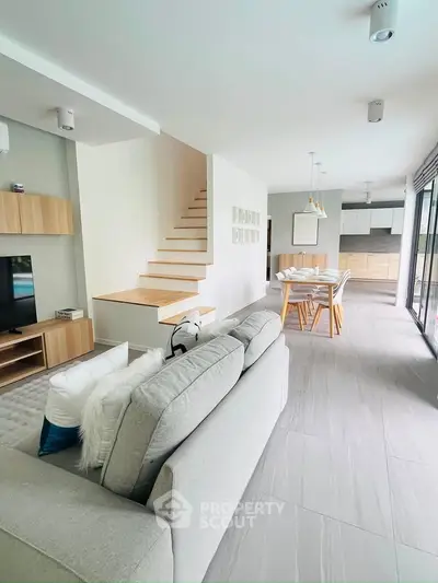 Modern open-plan living room with sleek staircase and dining area, featuring contemporary design and natural light.
