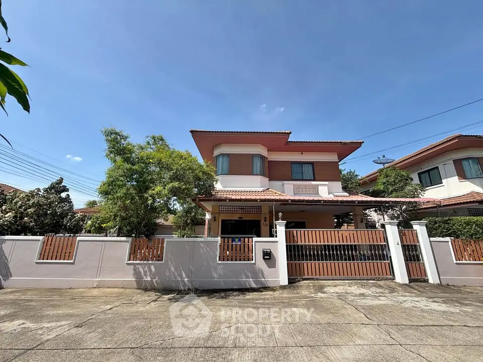 Charming two-story house with gated entrance and lush greenery in a serene neighborhood.