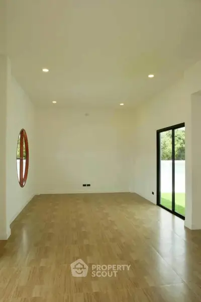 Spacious empty room with wooden flooring and large window overlooking greenery, ideal for customization.