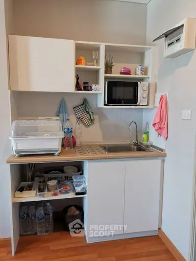 Compact kitchen with modern appliances and open shelving in cozy apartment.