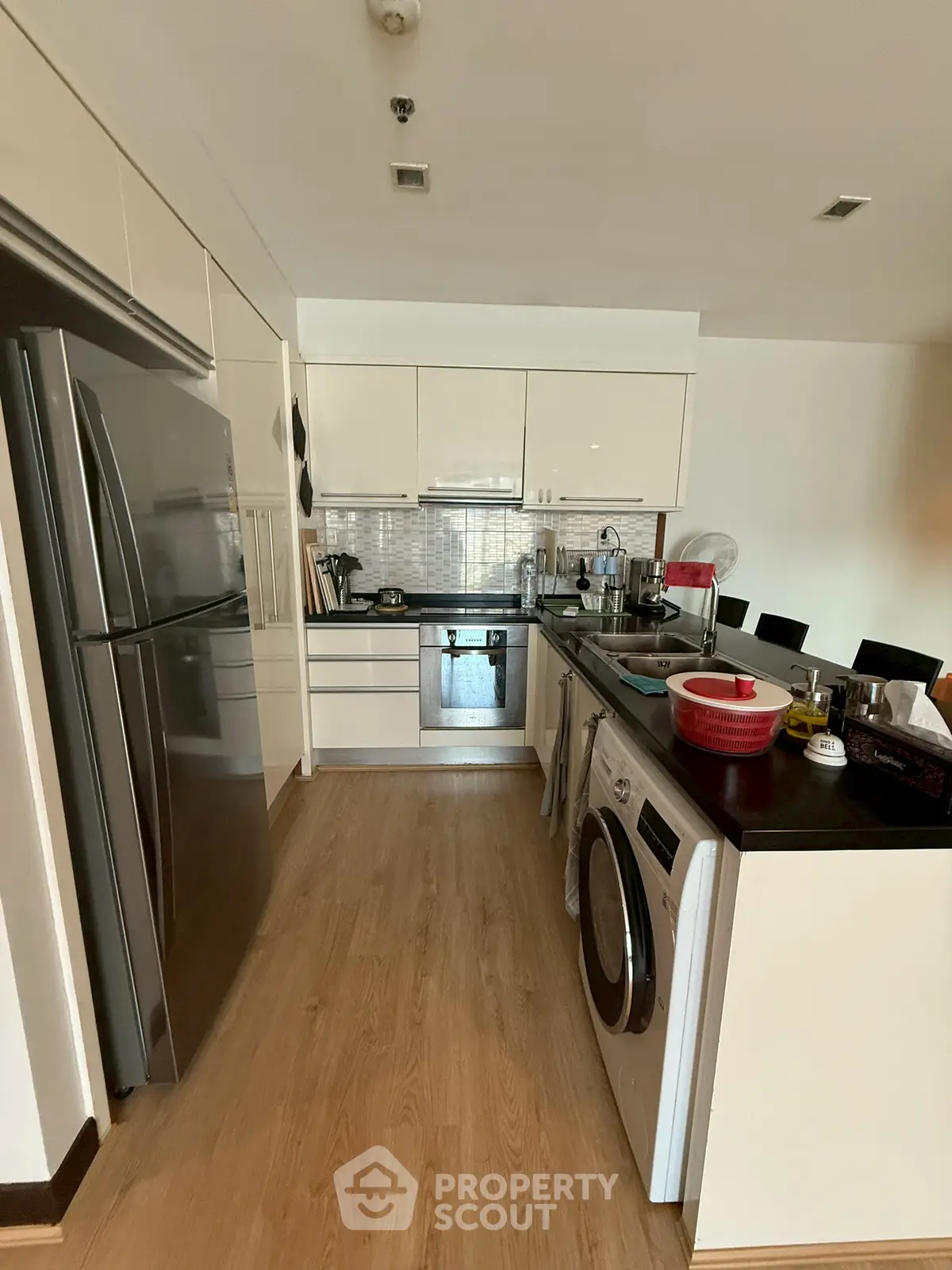 Modern kitchen with sleek appliances and wooden flooring, featuring a washing machine and oven.