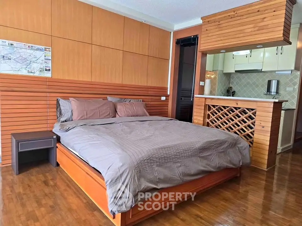 Spacious bedroom with wooden accents and open kitchen layout in modern apartment.