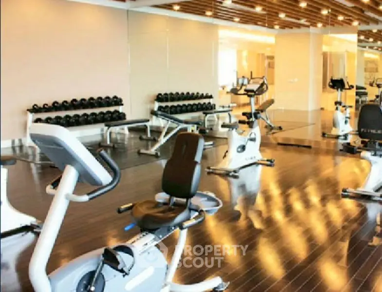 Luxurious gym with modern fitness equipment and sleek wooden flooring in upscale residential building.