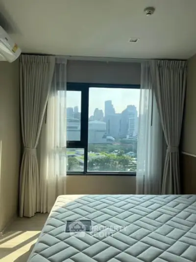 Bright bedroom with large window offering stunning city view, featuring modern decor and ample natural light.