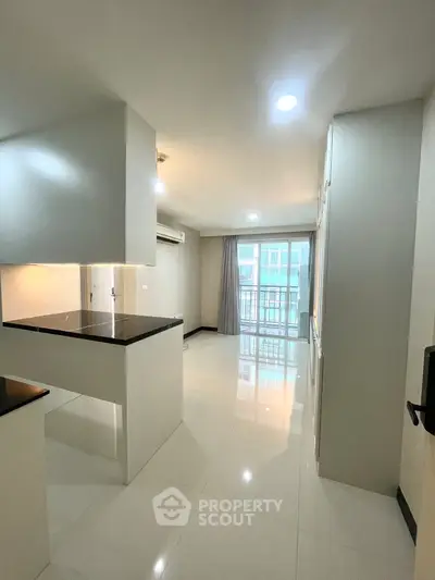 Modern open-layout kitchen with sleek countertops and bright living area leading to a balcony.