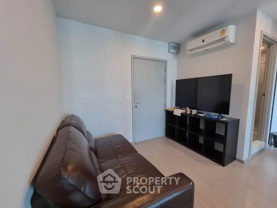 Modern living room with leather sofa and large TV, featuring sleek air conditioning unit.