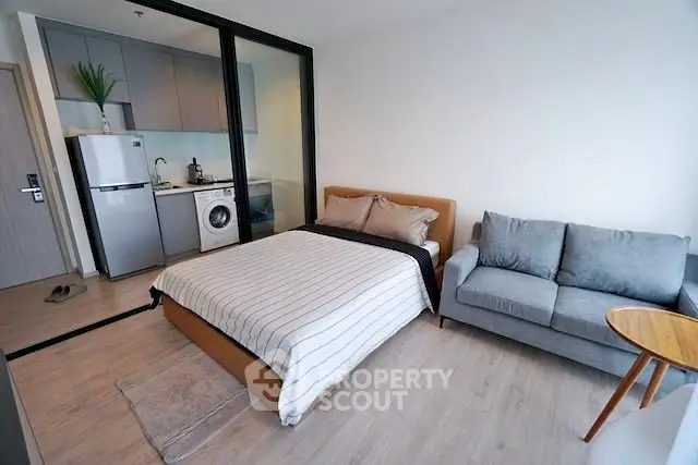 Modern studio apartment with cozy bedroom and compact kitchen featuring washing machine and fridge.