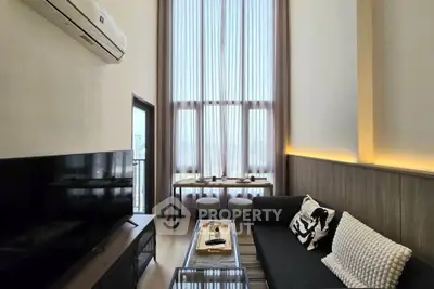 Modern living room with high ceilings and large windows, featuring stylish furniture and a sleek TV setup.