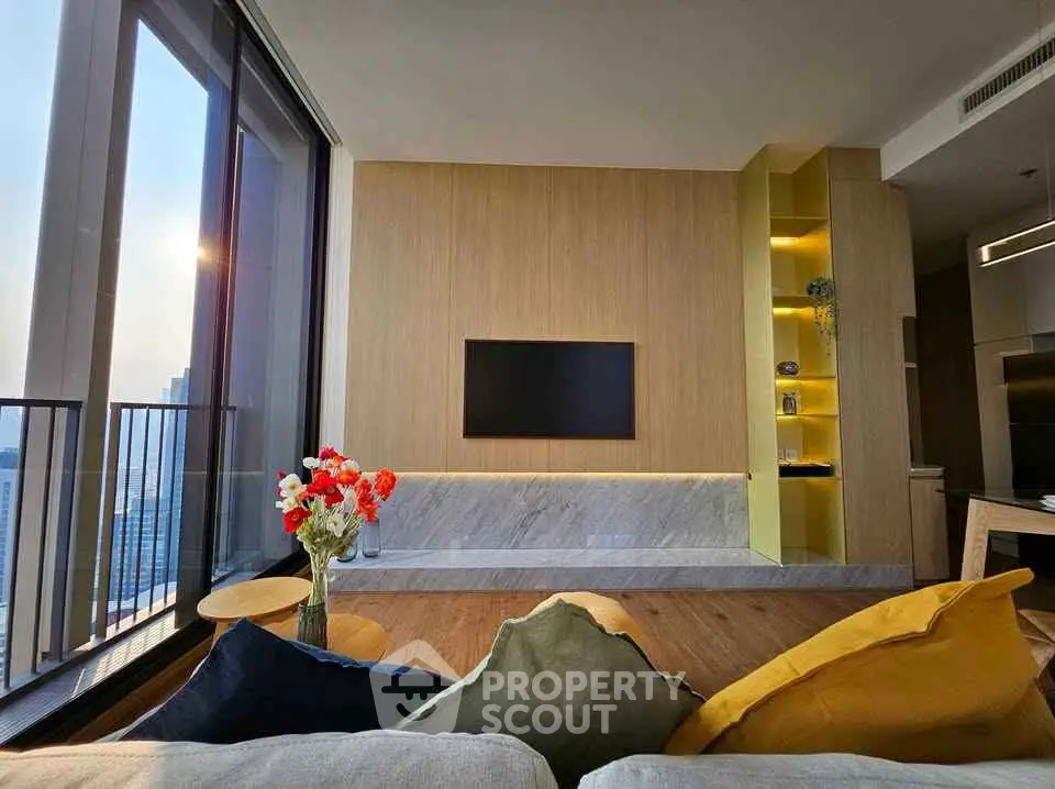Modern living room with large windows and stylish decor, featuring a wall-mounted TV and vibrant cushions.