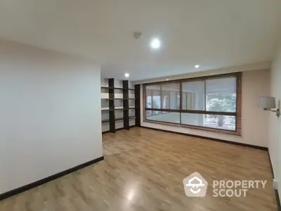 Spacious living room with large windows allowing ample natural light, elegant parquet flooring, and a modern built-in shelving unit.